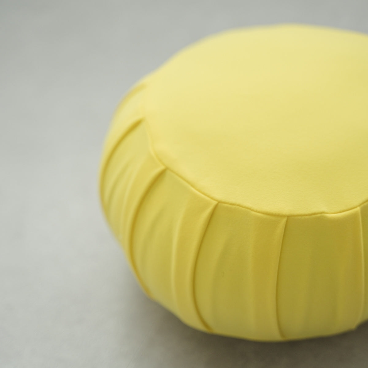 Close-up of a mimosa yellow Japanese meditation cushion (zafu), showing its pleated fabric on a modern floor for yoga.