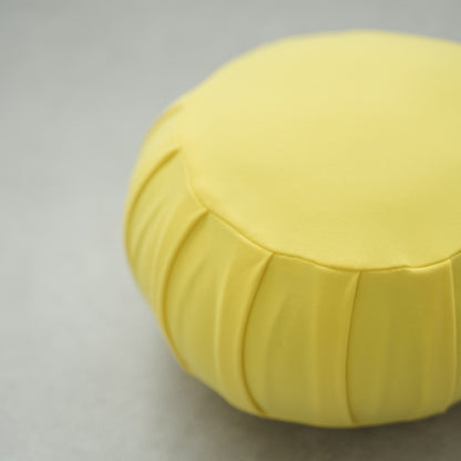 Close-up of a mimosa yellow Japanese meditation cushion (zafu), showing its pleated fabric on a modern floor for yoga.