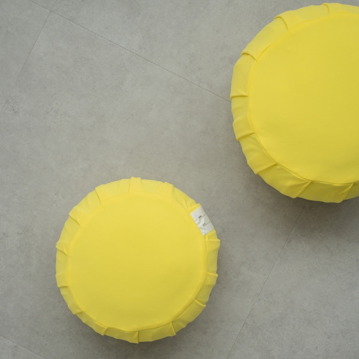 Two mimosa yellow Japanese meditation cushions (zafu) on a modern grey floor, arranged for a shared family zen ritual.
