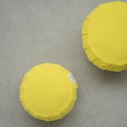 Two mimosa yellow Japanese meditation cushions (zafu) on a modern grey floor, arranged for a shared family zen ritual.