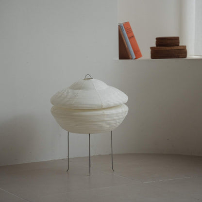 Modern Japanese paper lamp Gemini 01 placed on a tiled floor in a white Japandi room with books on a ledge behind it