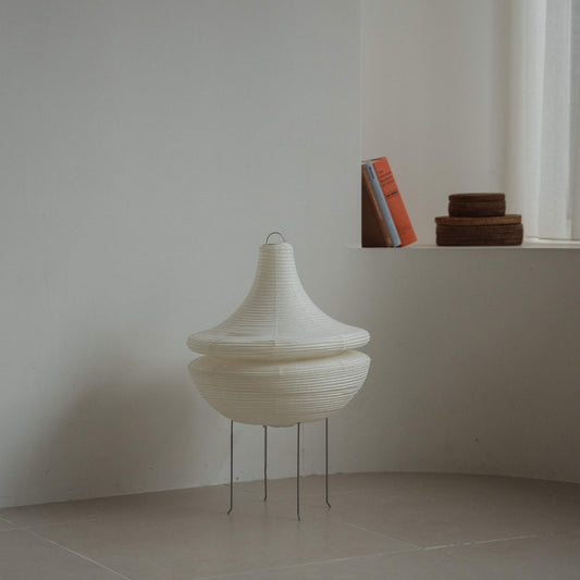 Modern Japanese paper floor lamp Gemini 02 standing on a tiled floor in a minimalist white room with books in the background