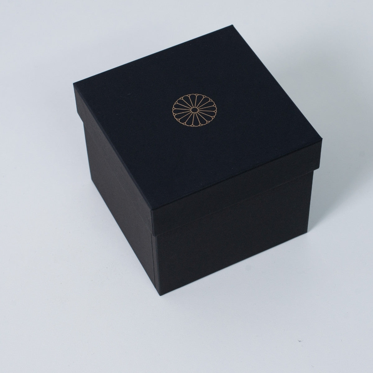 Closed black square Ninshu's gift box for Japanese pottery, featuring a gold imperial chrysanthemum crest on the lid.