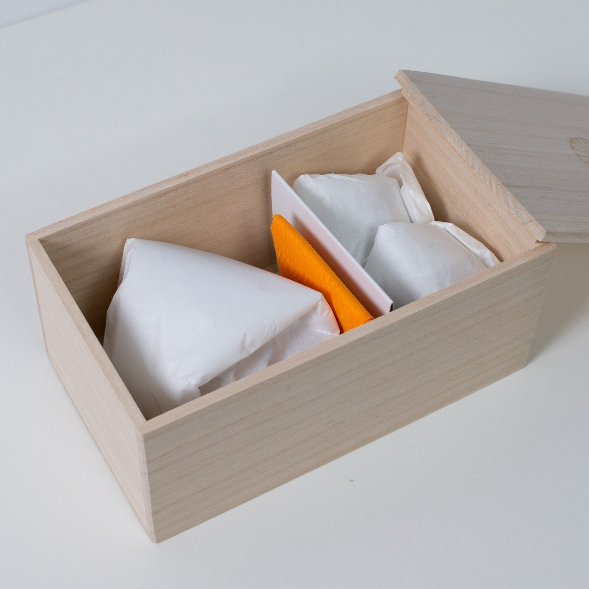 Rechteckige offene Holzkiste von Ninshu für ein japanisches Keramik-Sake-Set, mit eingewickelten Gefäßen und einem gelben Tuch im Inneren.