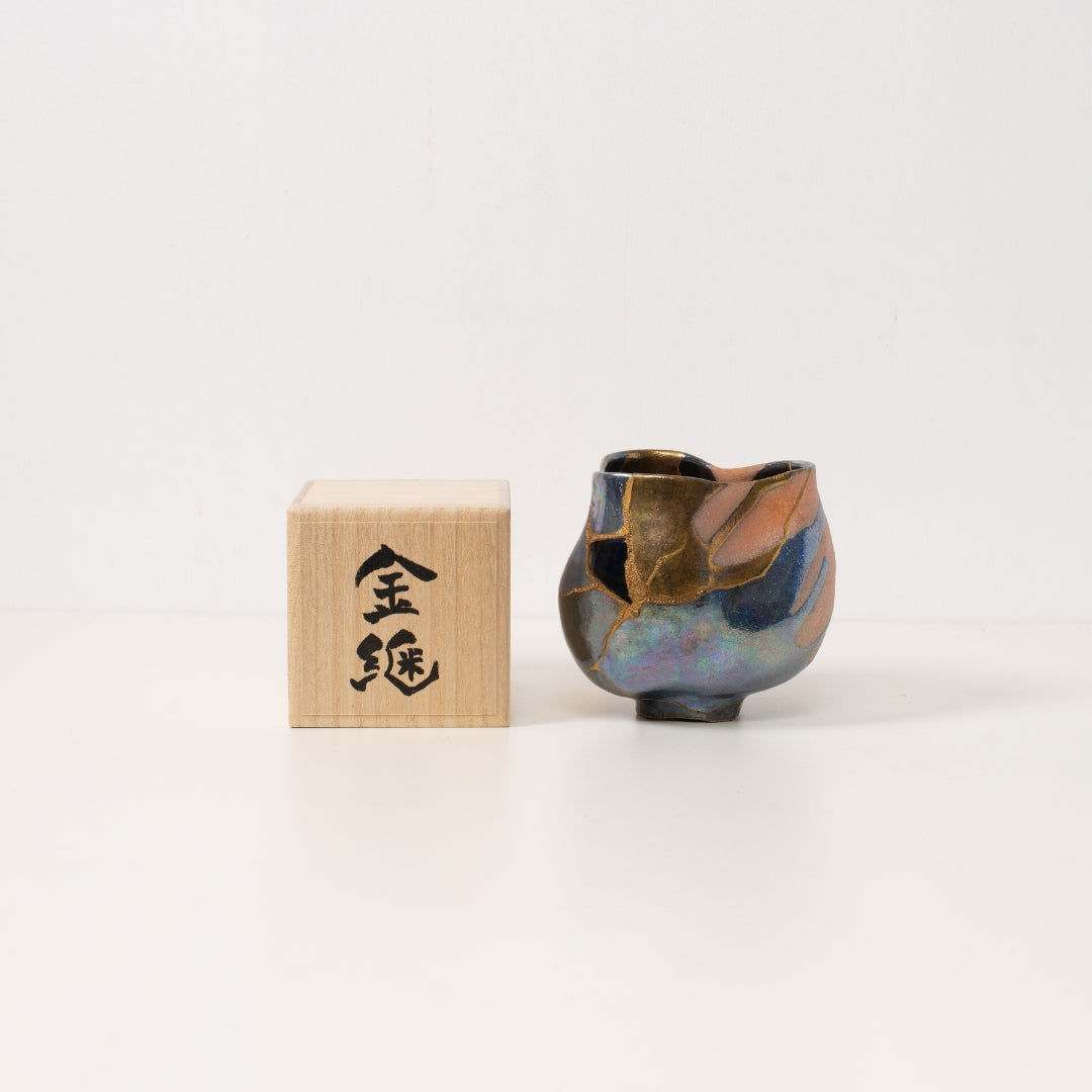 An iridescent kintsugi matcha bowl stands beside a paulownia wood gift box representing beautiful wabi sabi pottery art