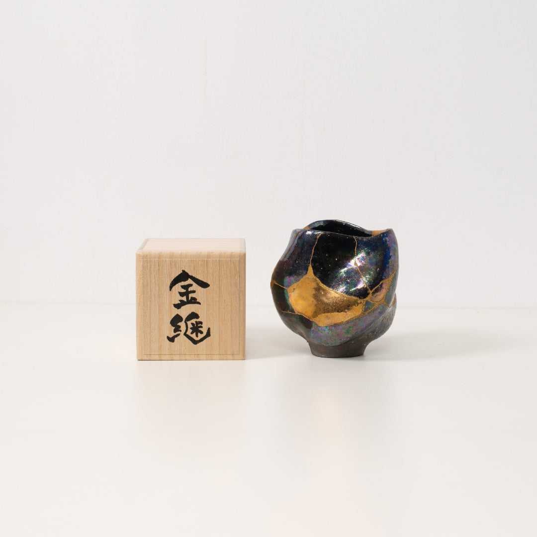 An iridescent kintsugi matcha bowl sits next to a wooden japanese gift box ready to be given as a unique artwork