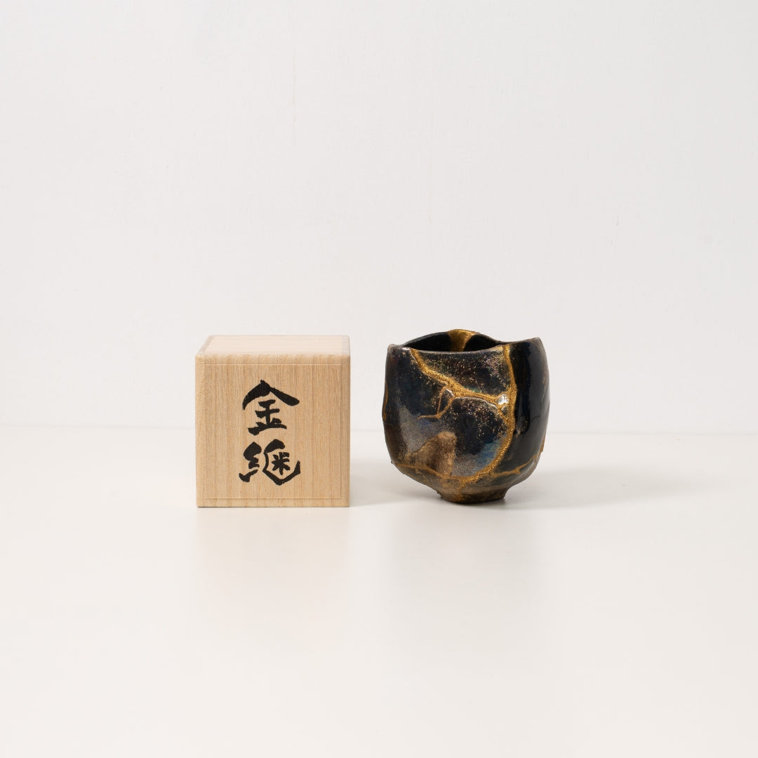 A black kintsugi matcha bowl sits beside a wooden japanese gift box showcasing resilient pottery art