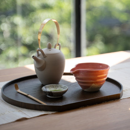 Pink Japanese matcha bowl with spout and tea tools on a dark tray by a sunny window, set for a peaceful authentic tea time.