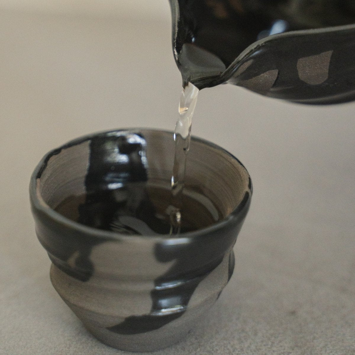 Sake wird aus einer japanischen Sumi Black Katakuchi-Sake-Karaffe in einen passenden Sake-Becher (Ochoko) gegossen, um Premium-Sake zu servieren.