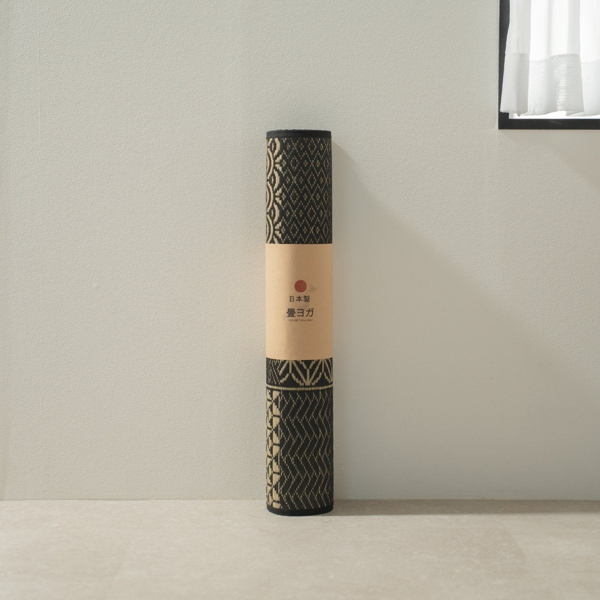 Rolled Japanese Tatami Yoga Mattress "Ed Plain" Black standing by a white wall, ready for your daily mindful practice.