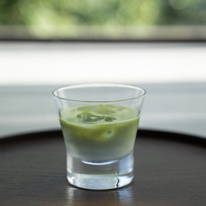Iced matcha latte in a glass on a dark wood tray for a refreshing break with a green background.