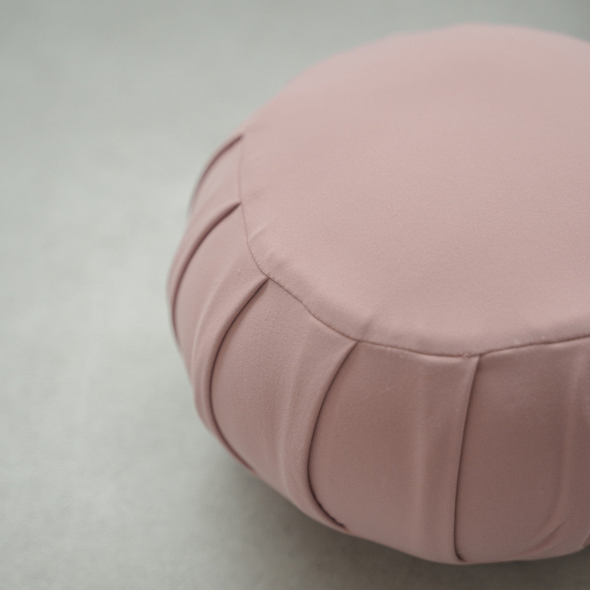 Close-up of a rose Japanese meditation cushion (zafu) showing fabric details on a modern floor for relaxing home yoga.