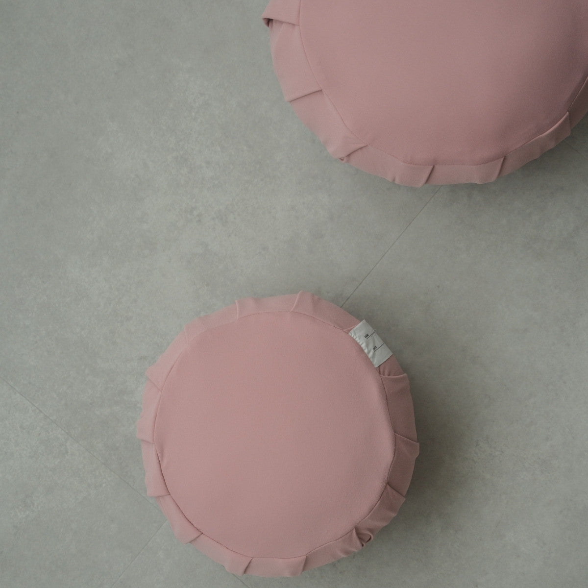 Two rose Japanese meditation cushions (zafu) on a modern grey floor, prepared for shared family mindfulness.