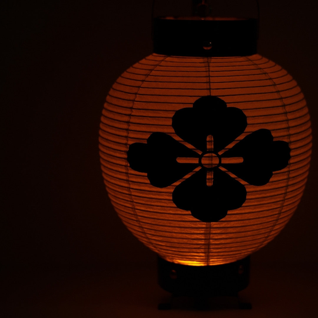 Close up of a Japanese washi paper lantern with a flower crest glowing in a dark space for a calm atmosphere.