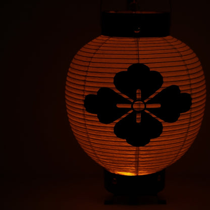 Close up of a Japanese washi paper lantern with a flower crest glowing in a dark space for a calm atmosphere.