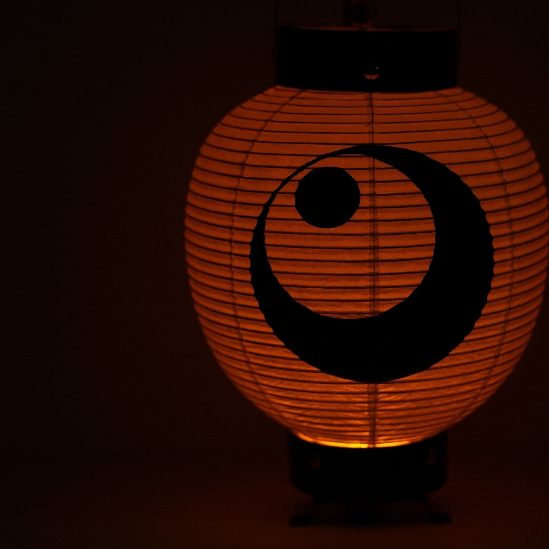 Close up of a handcrafted chochin lantern emitting soft light in the dark showing the delicate washi paper texture.