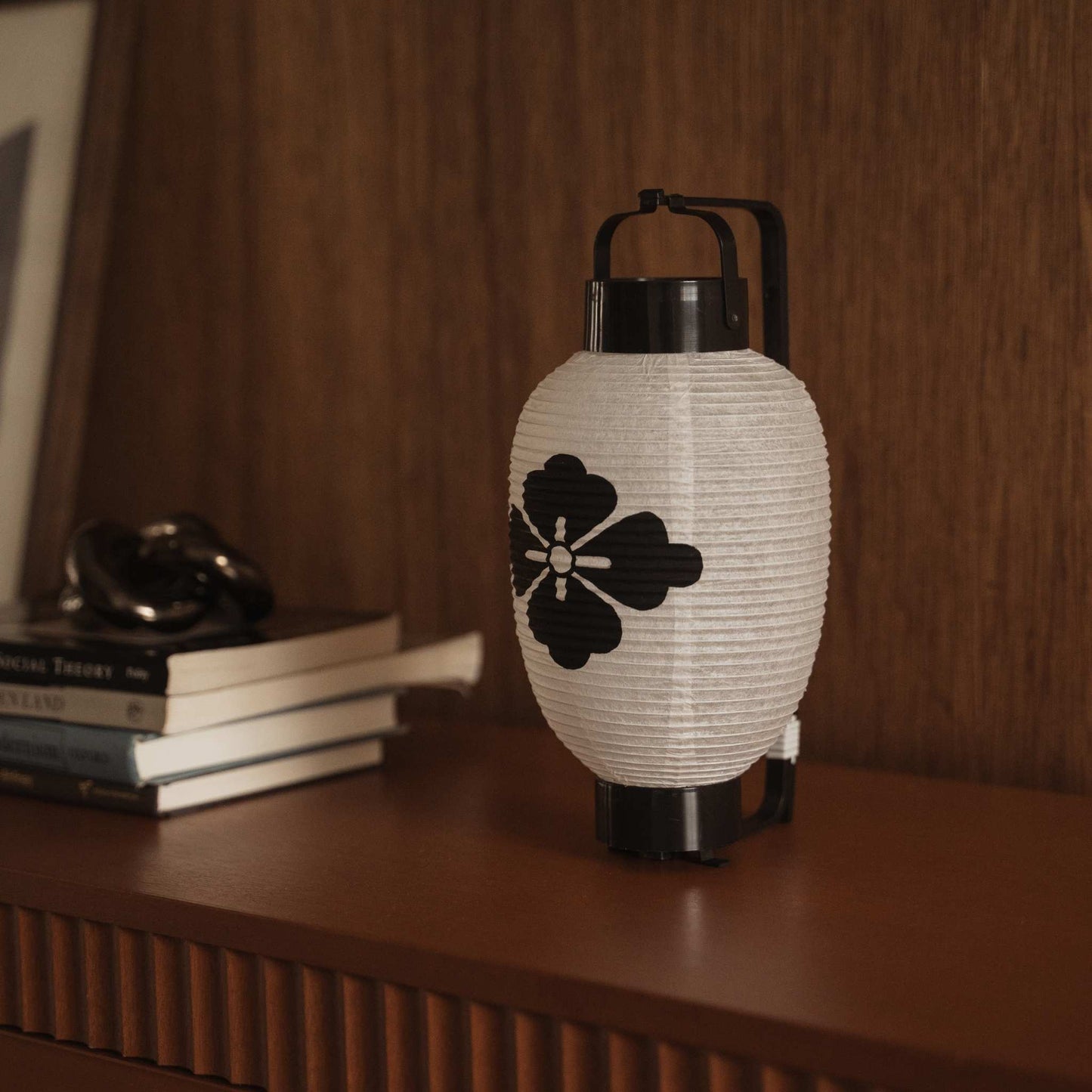 Traditional japanese paper lantern with flower diamond crest placed next to books on a wooden console table.
