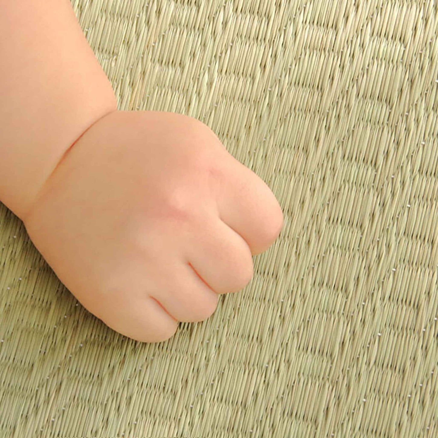 Baby hand resting on a natural tatami mat showing the smooth texture safe for sensitive skin.