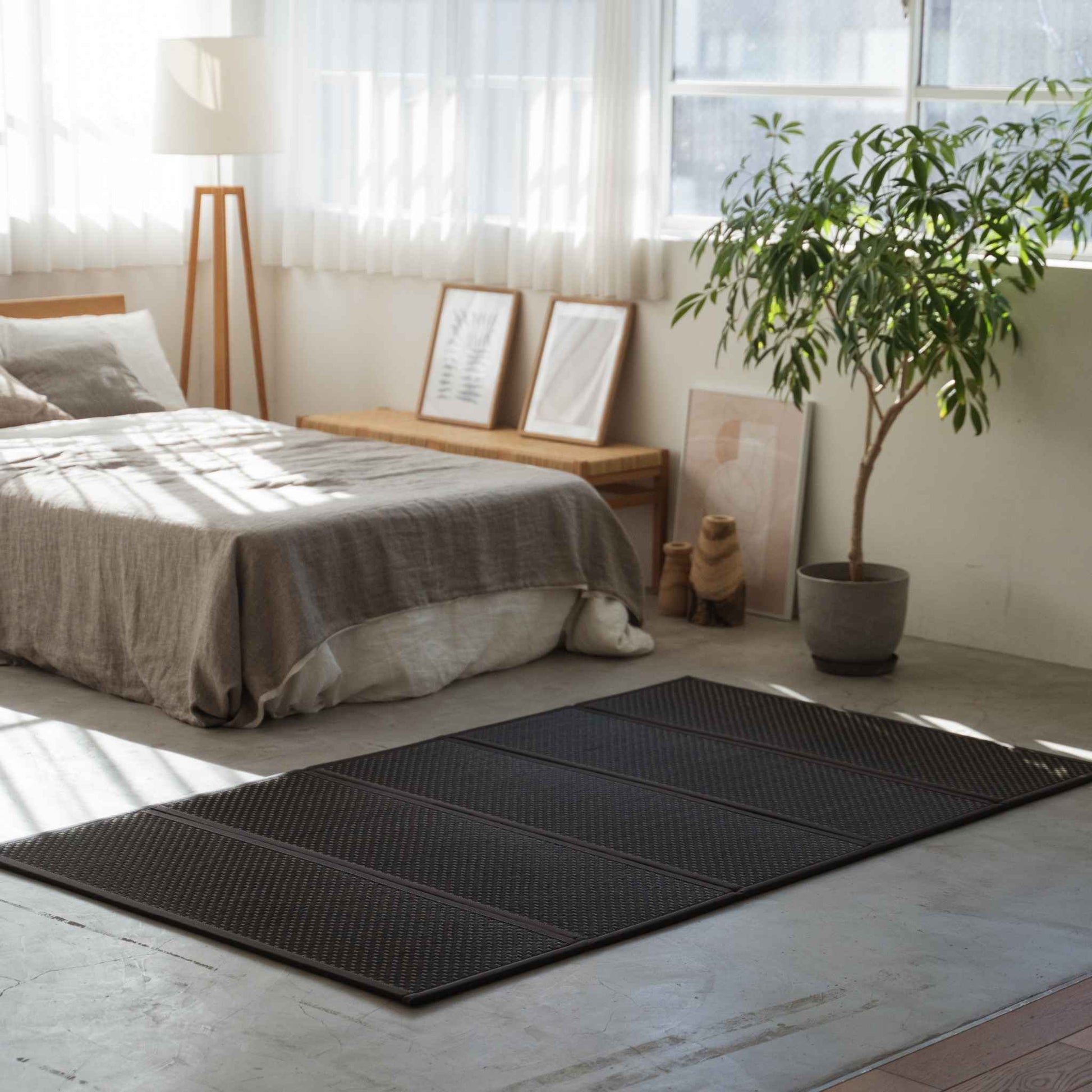 Black semi-double tatami mat on a concrete bedroom floor providing a modern zen foundation for a futon.