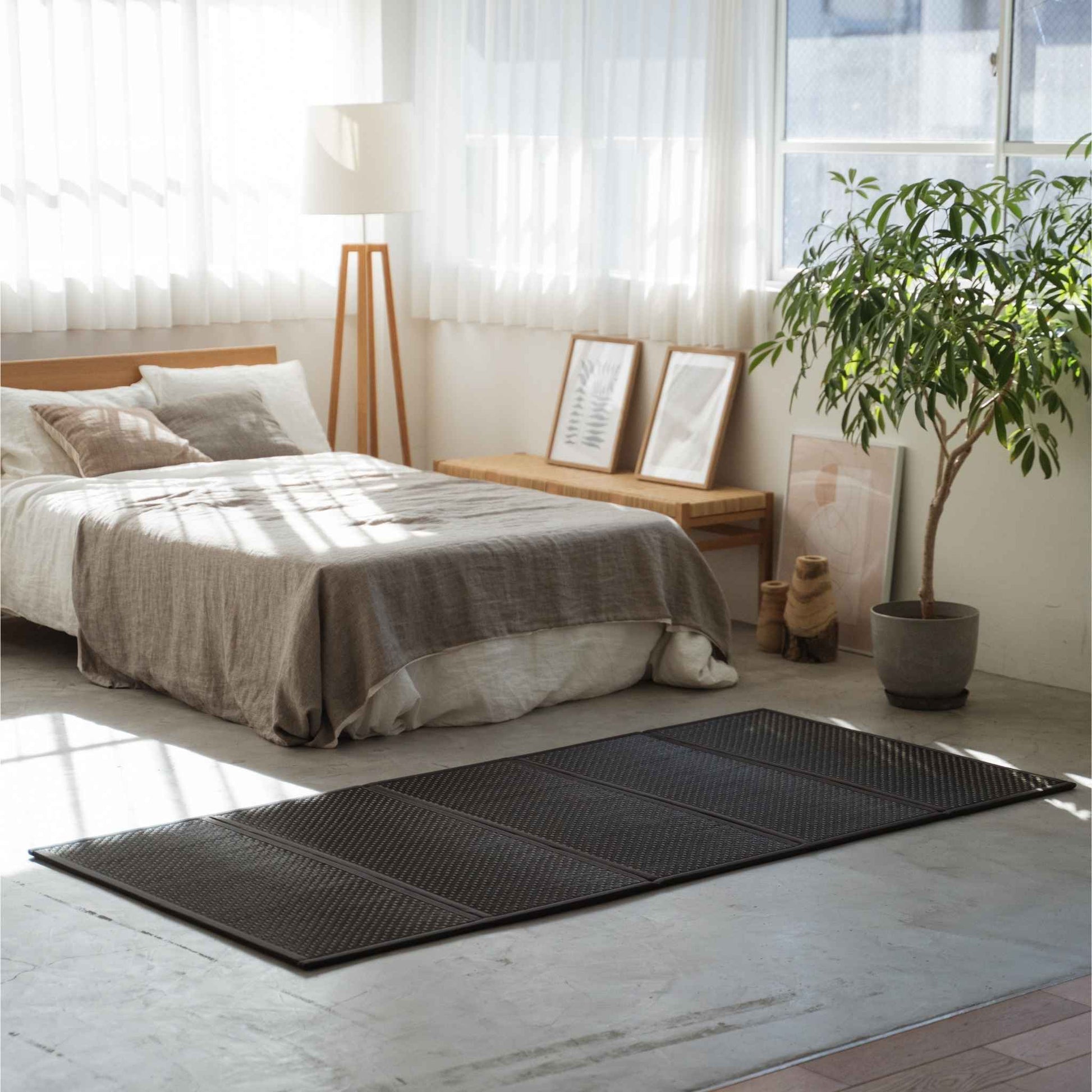 Single black tatami mat placed on a concrete floor in a sunlit room offering a minimalist Japanese decor vibe.