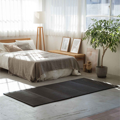 Single black tatami mat placed on a concrete floor in a sunlit room offering a minimalist Japanese decor vibe.