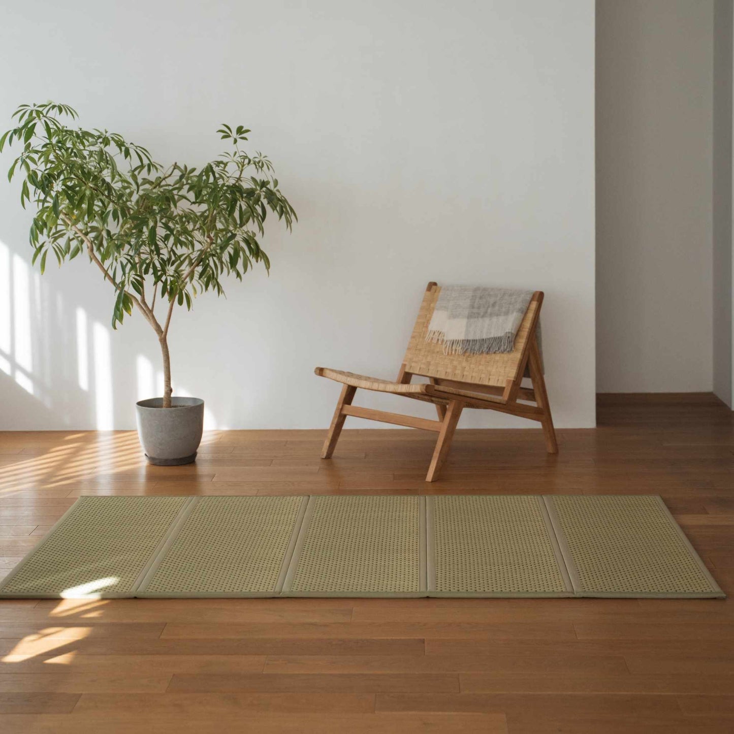 Green double tatami mat placed on a wooden floor next to a chair and plant for minimalist Japanese decor.