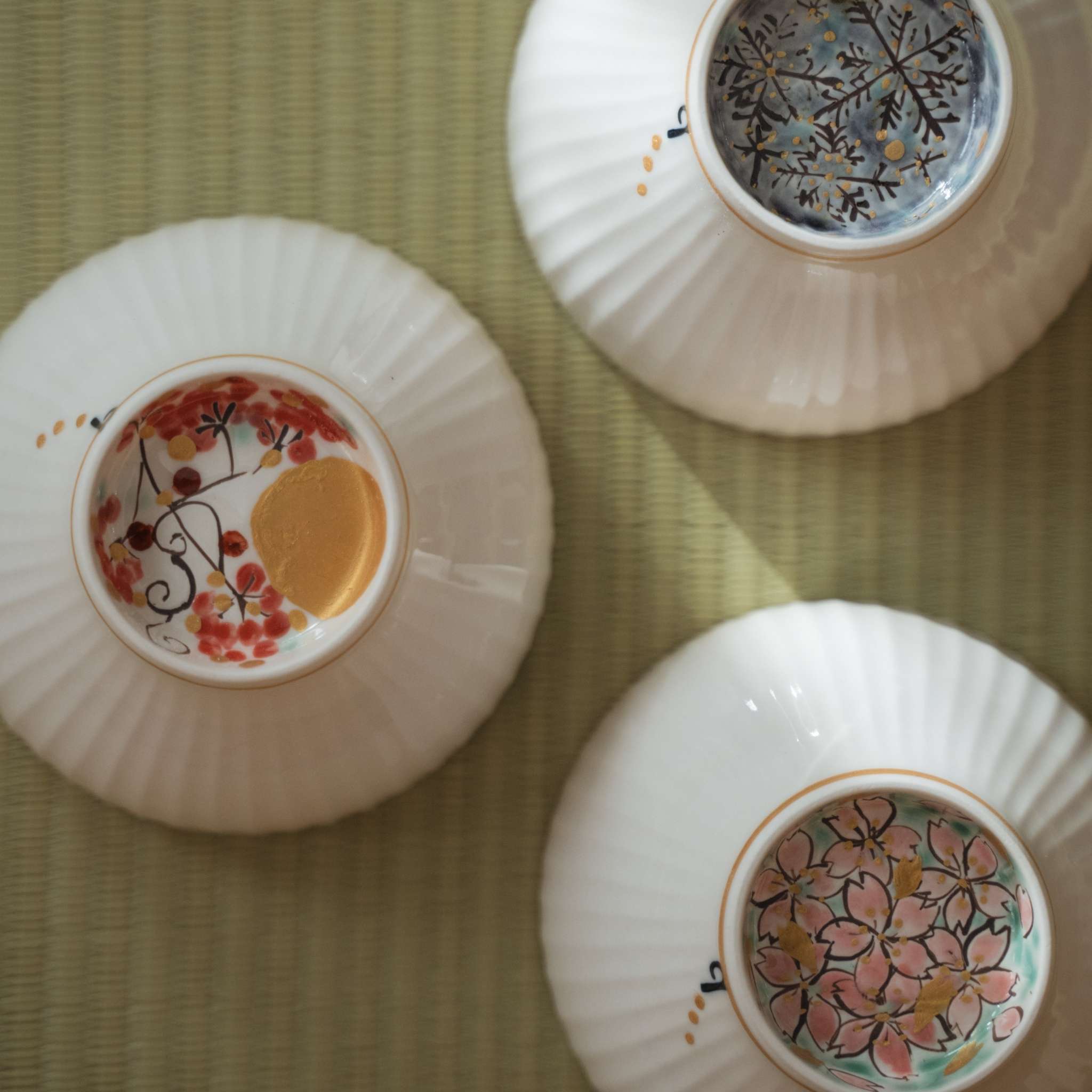 Three upside down japanese matcha bowls on a tatami mat showing moon snow and flower designs on their bases.