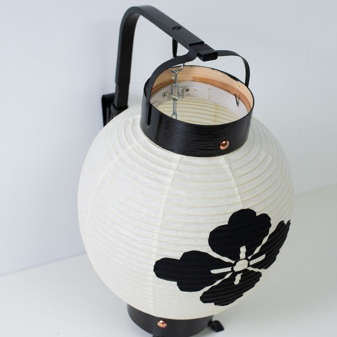 Detailed view of a miniature chochin lantern with a flower crest showing the traditional bamboo handle and black frame.