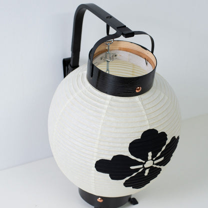 Detailed view of a miniature chochin lantern with a flower crest showing the traditional bamboo handle and black frame.