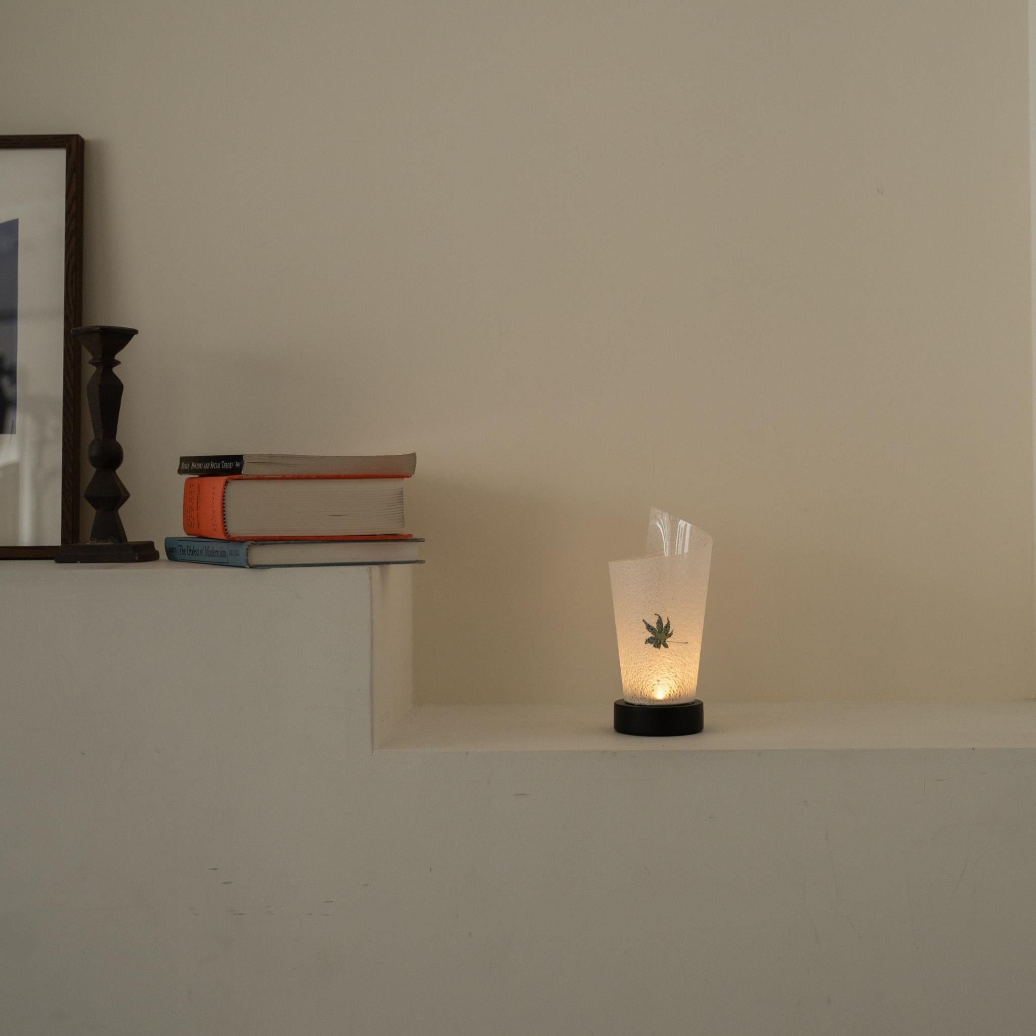 Lit Japanese paper table lamp "Maki" Momiji Leaf glowing warmly as an ambient lamp on a white console table in a Japandi living room.