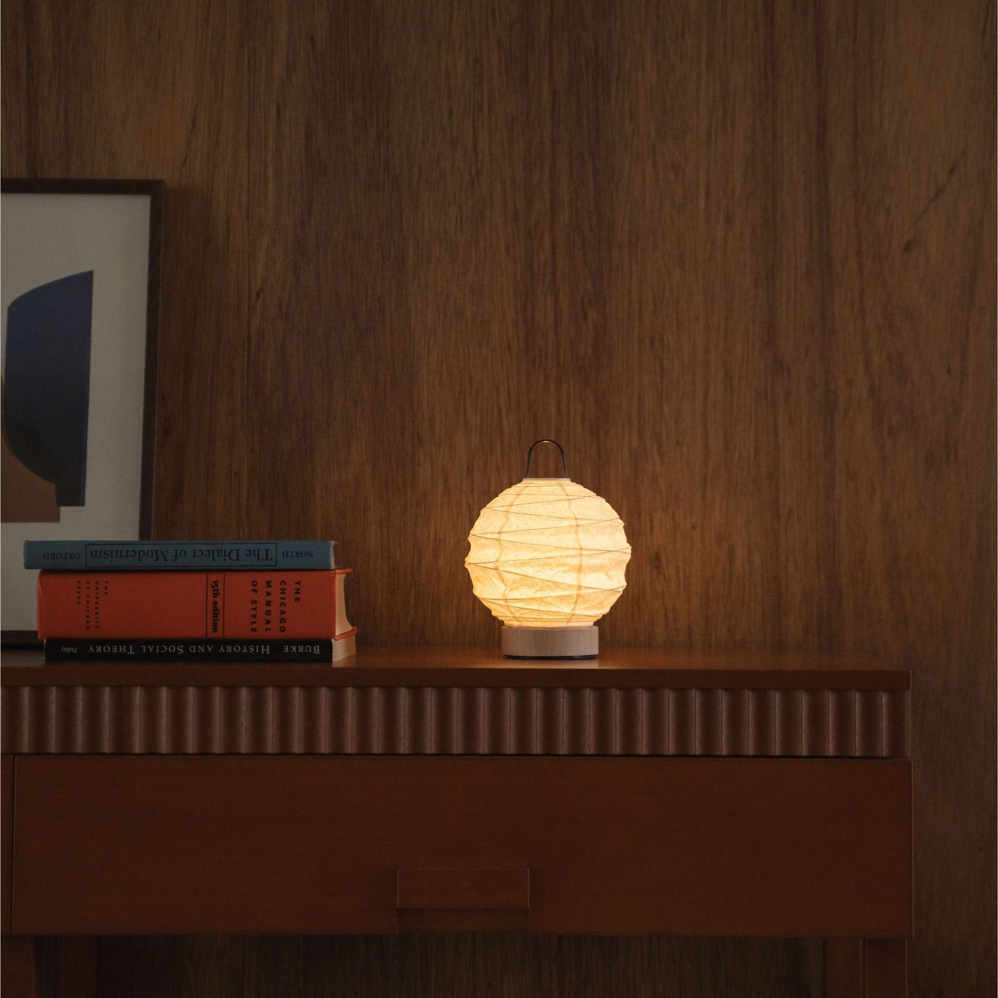 Lit round Japanese paper table lamp "Yuhi" providing warm light on a mid-century modern wooden console in a living room.