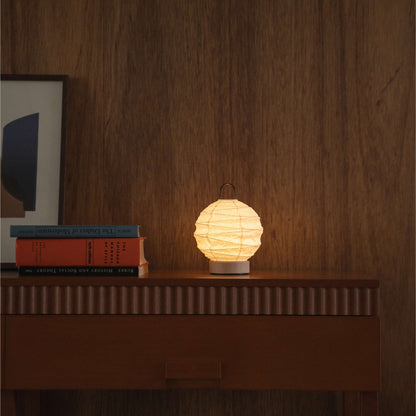 Lit round Japanese paper table lamp "Yuhi" providing warm light on a mid-century modern wooden console in a living room.