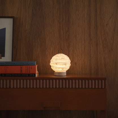 Lit round Japanese paper table lamp "Yuhi" Rabbit providing warm light on a mid-century modern wooden console in a living room.