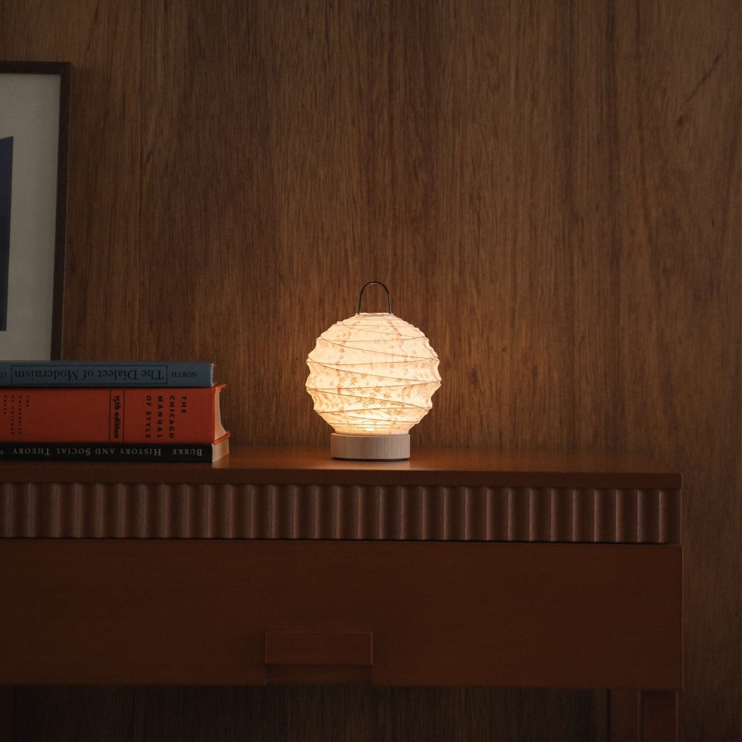 Lit round Japanese paper table lamp "Yuhi" Sakura providing warm light on a mid-century modern wooden console in a living room.