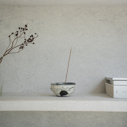 White and black Japanese incense burner on a light shelf with books, setting a serene mood for a morning yoga routine.