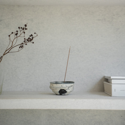 White and black Japanese incense burner on a light shelf with books, setting a serene mood for a morning yoga routine.