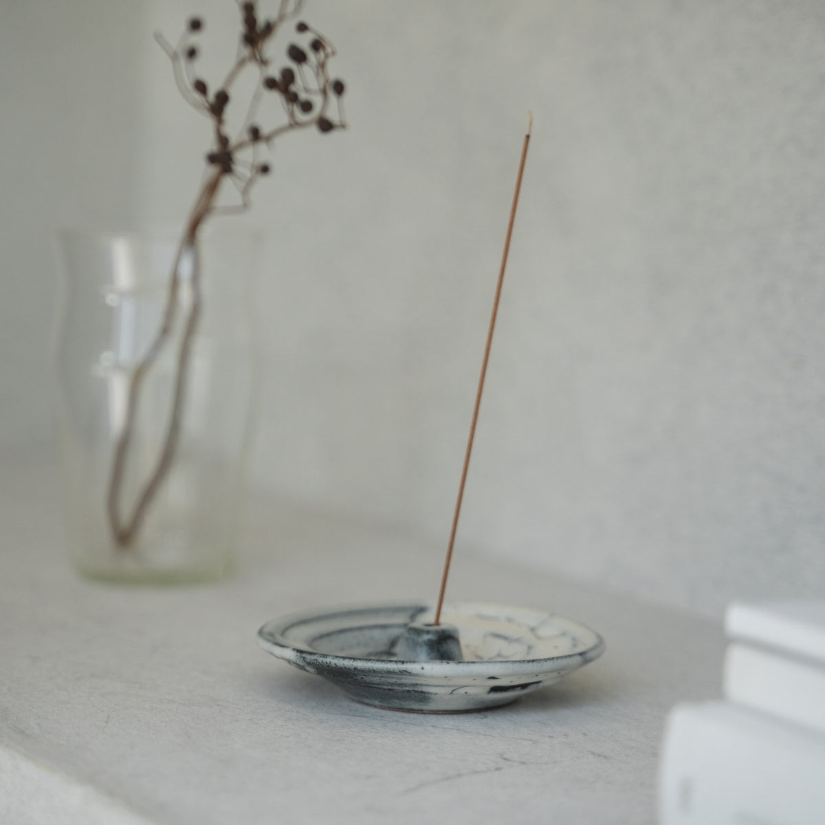 White and grey Japanese incense holder with a lit stick on a light tabletop, creating serenity for a morning meditation.