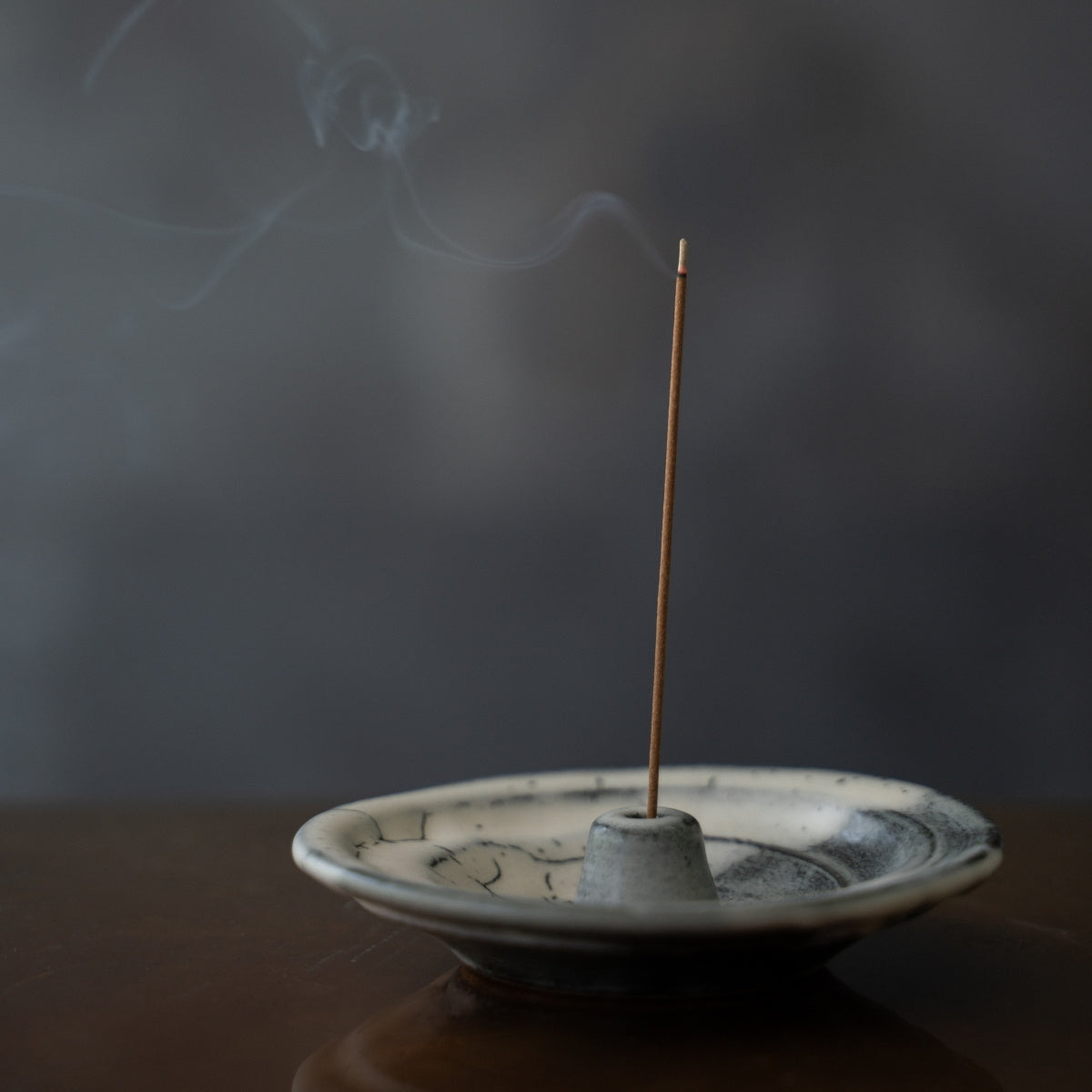 Cloud glazed Japanese incense holder on a dark table with swirling smoke, enhancing focus during a morning yoga practice.