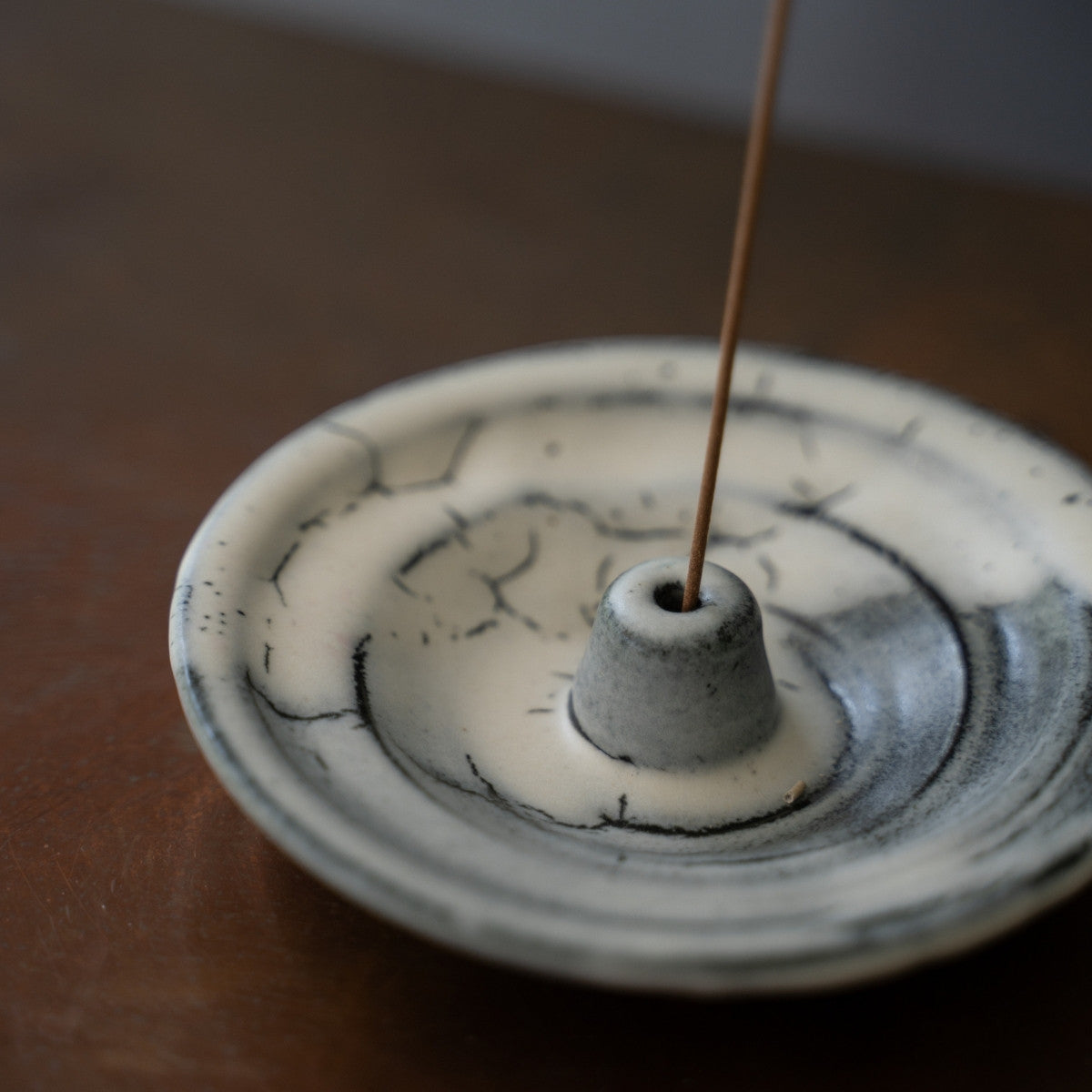 High-angle view of a white Japanese incense holder on a wood surface, catching ash safely during a serene meditation.