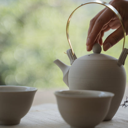 Håndbrygning af te med en hvid japansk kyusu tekande ved et lyst vindue for te-entusiaster, der starter deres mindfulde morgen.