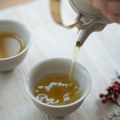 Fyldning af hvide japanske tekopper med en kyusu på et lyst bord til te-entusiaster, der nyder en beroligende eftermiddagspause.