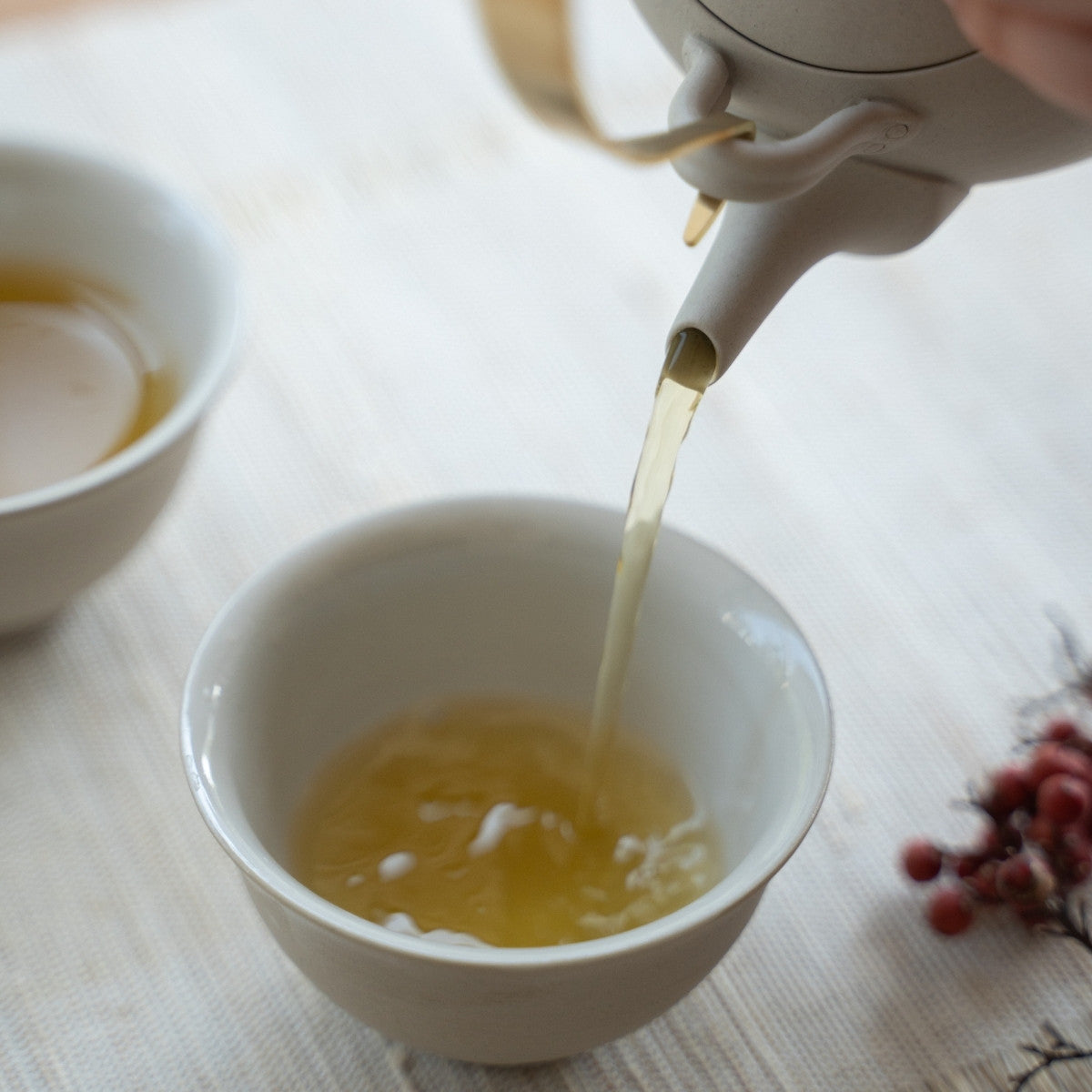 Hældning af en frisk bryg fra et hvidt japansk tesæt "Donguri" i et solrigt rum for teelskere, der nyder en aromatisk velvære.