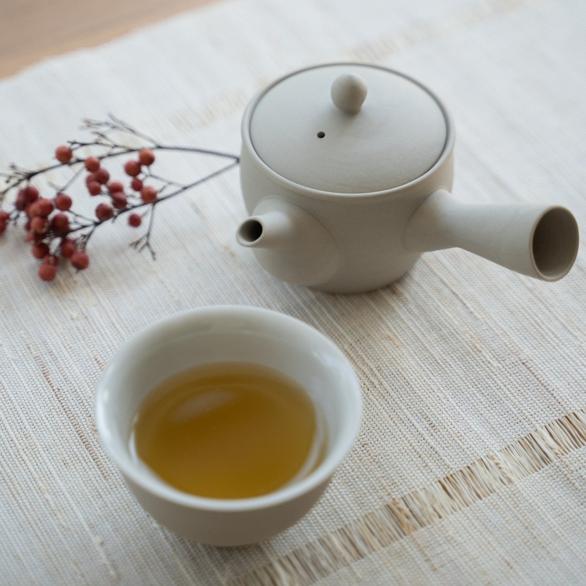 Hvidt japansk tesæt "Fuyo" med brygget te på en linned måtte til teentusiaster, der nyder et beroligende solo-ritual.