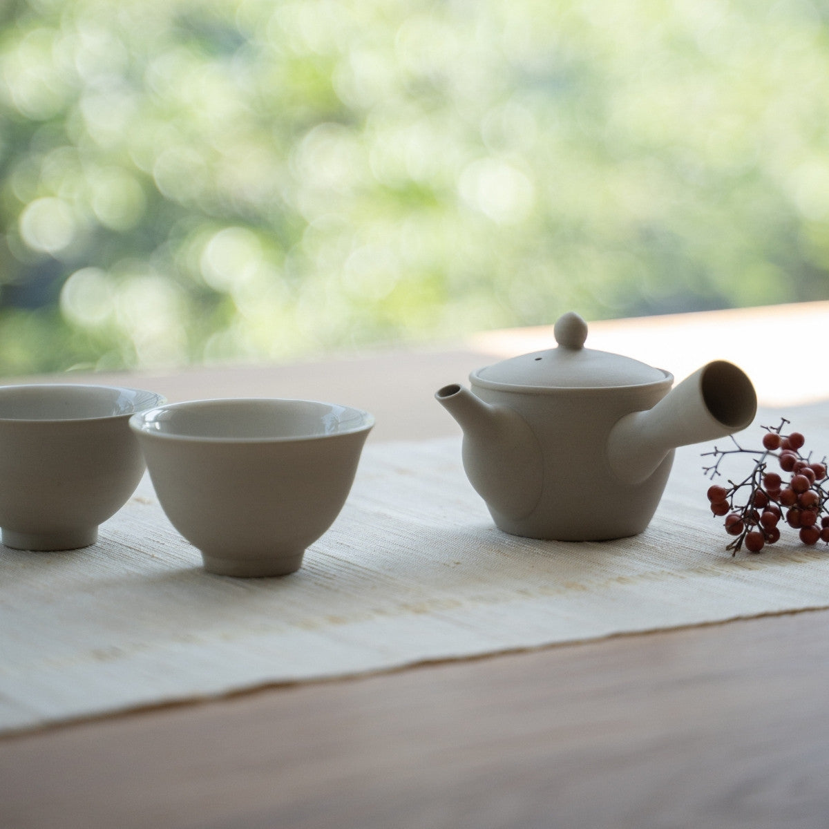 Hvid kyusu tekande "Fuyo" og japanske tekopper på et solbeskinnet bord for wellness-søgende, der nyder en mindful samtale.