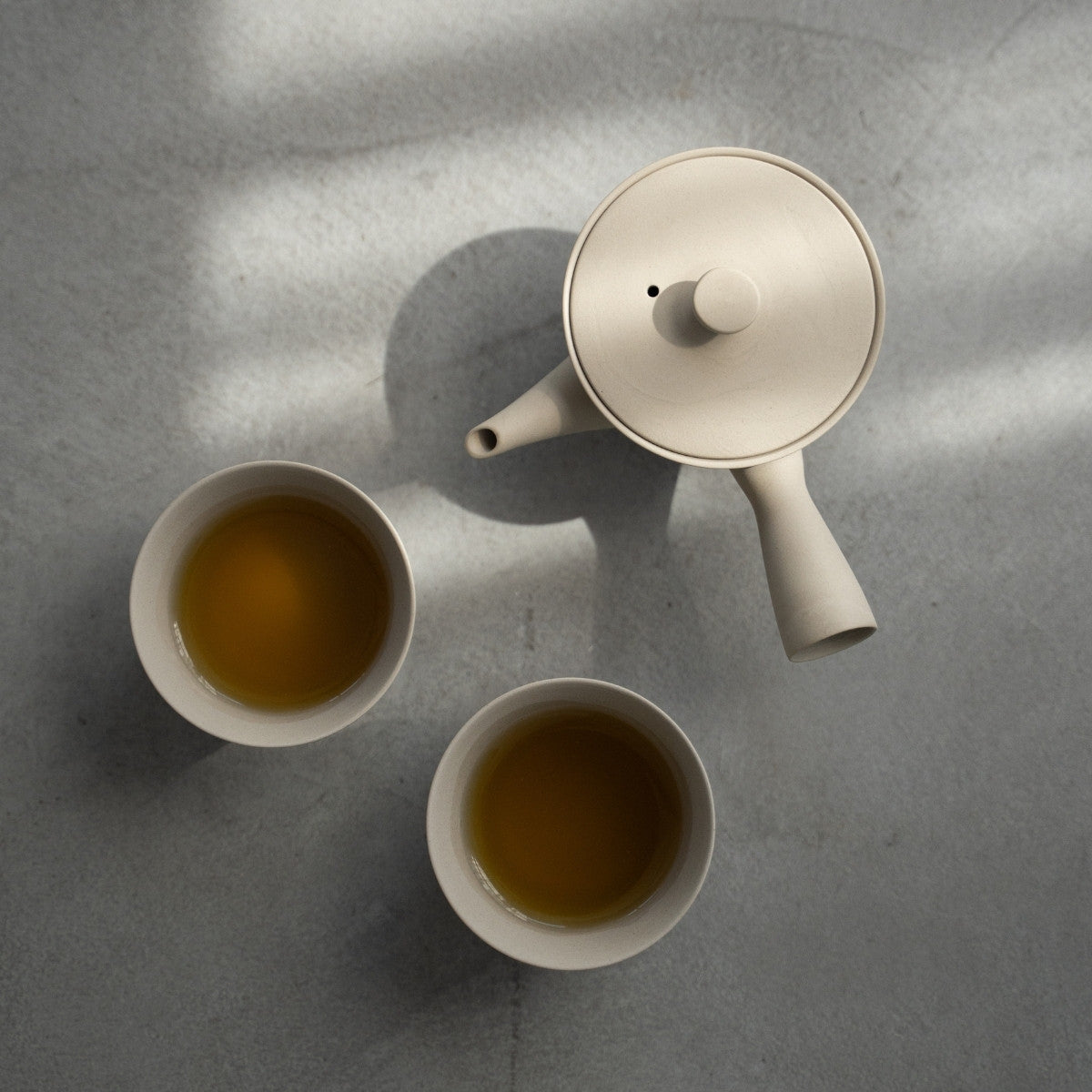 Hvidt japansk tesæt "Sencha" med brygget te på en betonoverflade til minimalister, der nyder et roligt wellness-ritual.