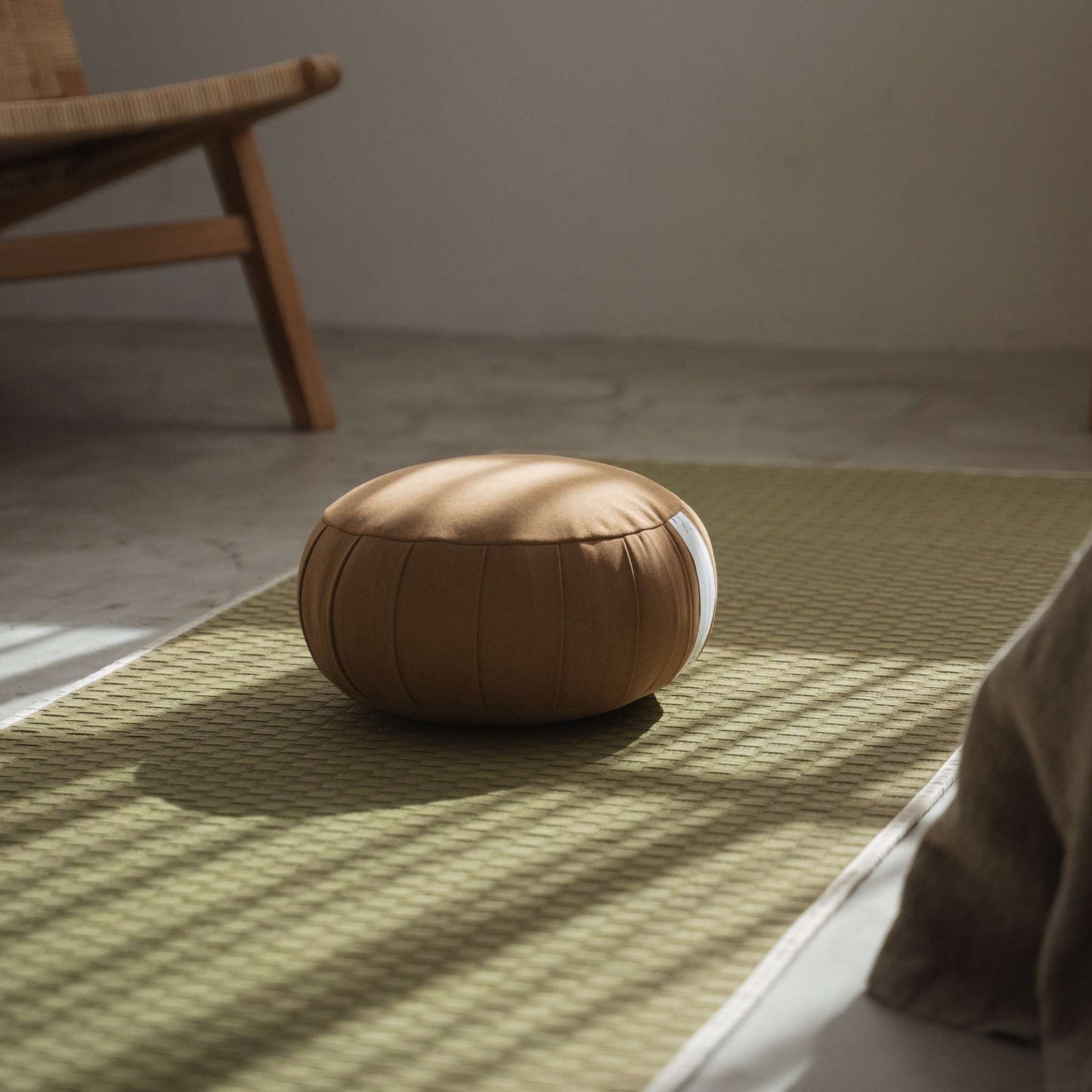 Authentic caramel brown zafu meditation cushion resting on a traditional tatami mat with natural window light.