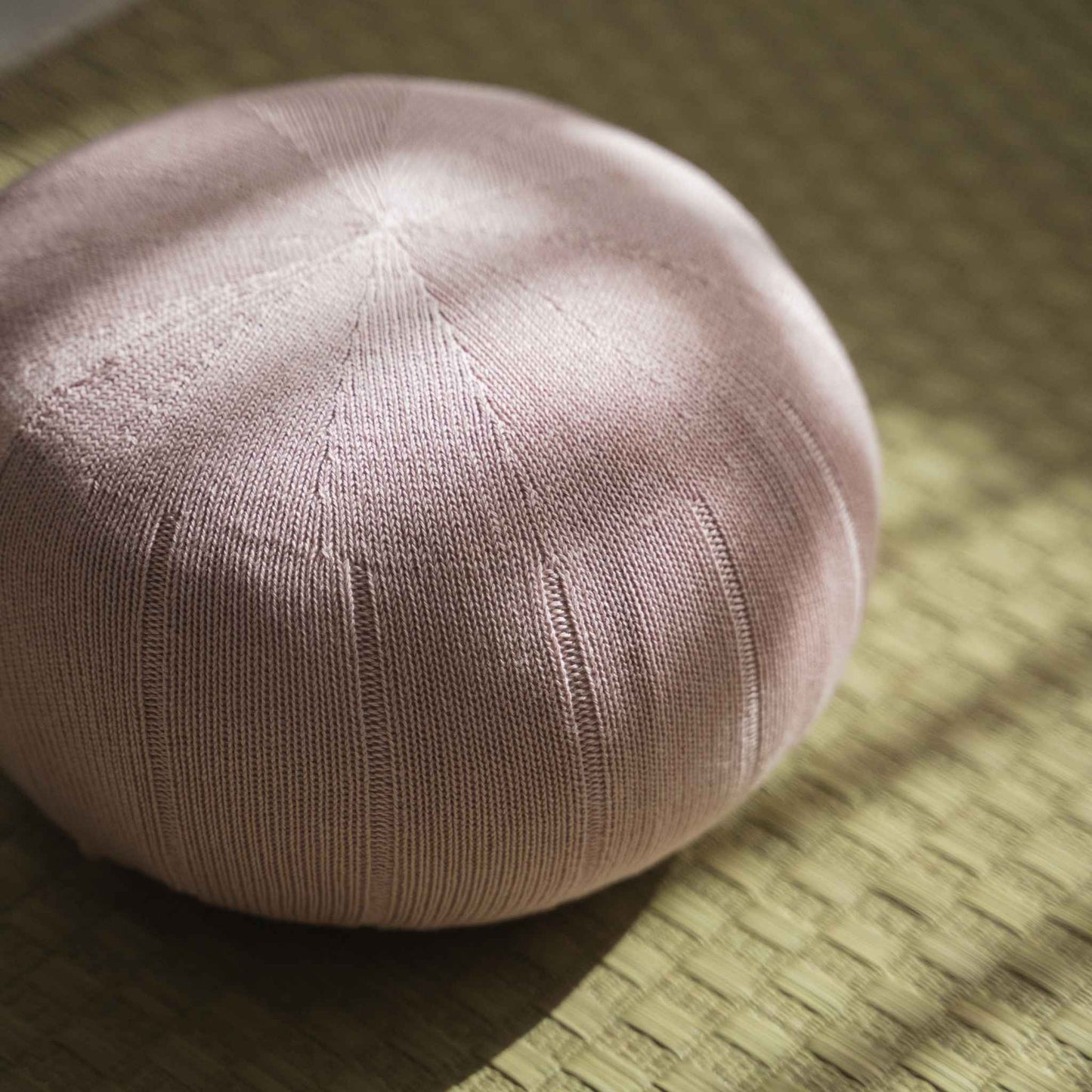Close up of misty rose zafu meditation cushion showing organic cotton knit texture on a tatami mat.