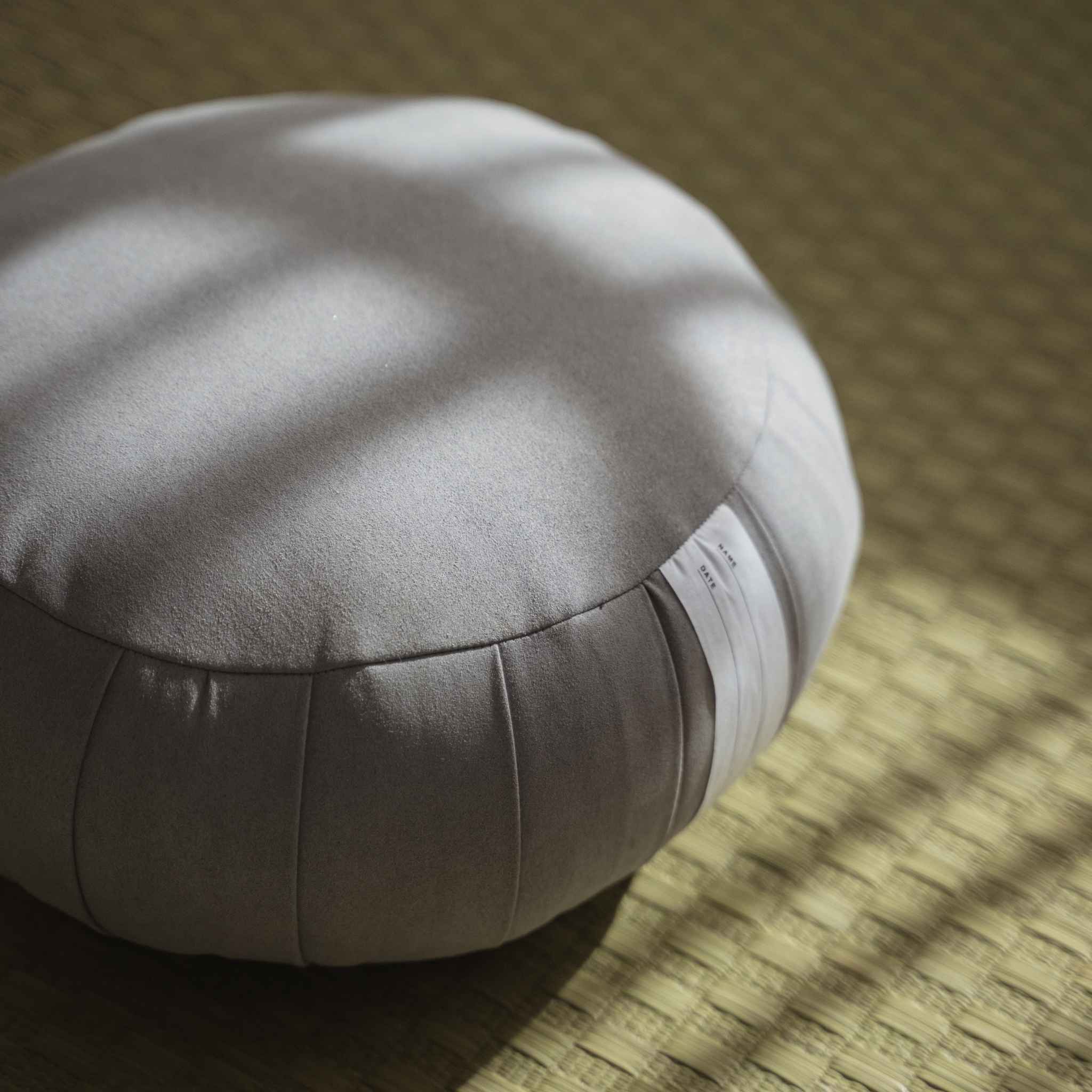 Detailed view of silver gray zafu meditation cushion highlighting the suede like fabric texture on a tatami mat.