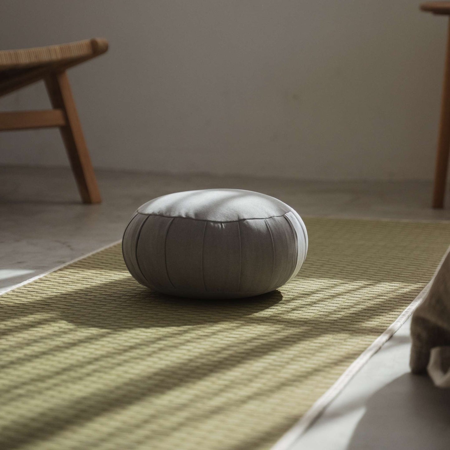 Silver gray zafu meditation cushion placed on a green tatami mat in a minimalist zen space for mindfulness.