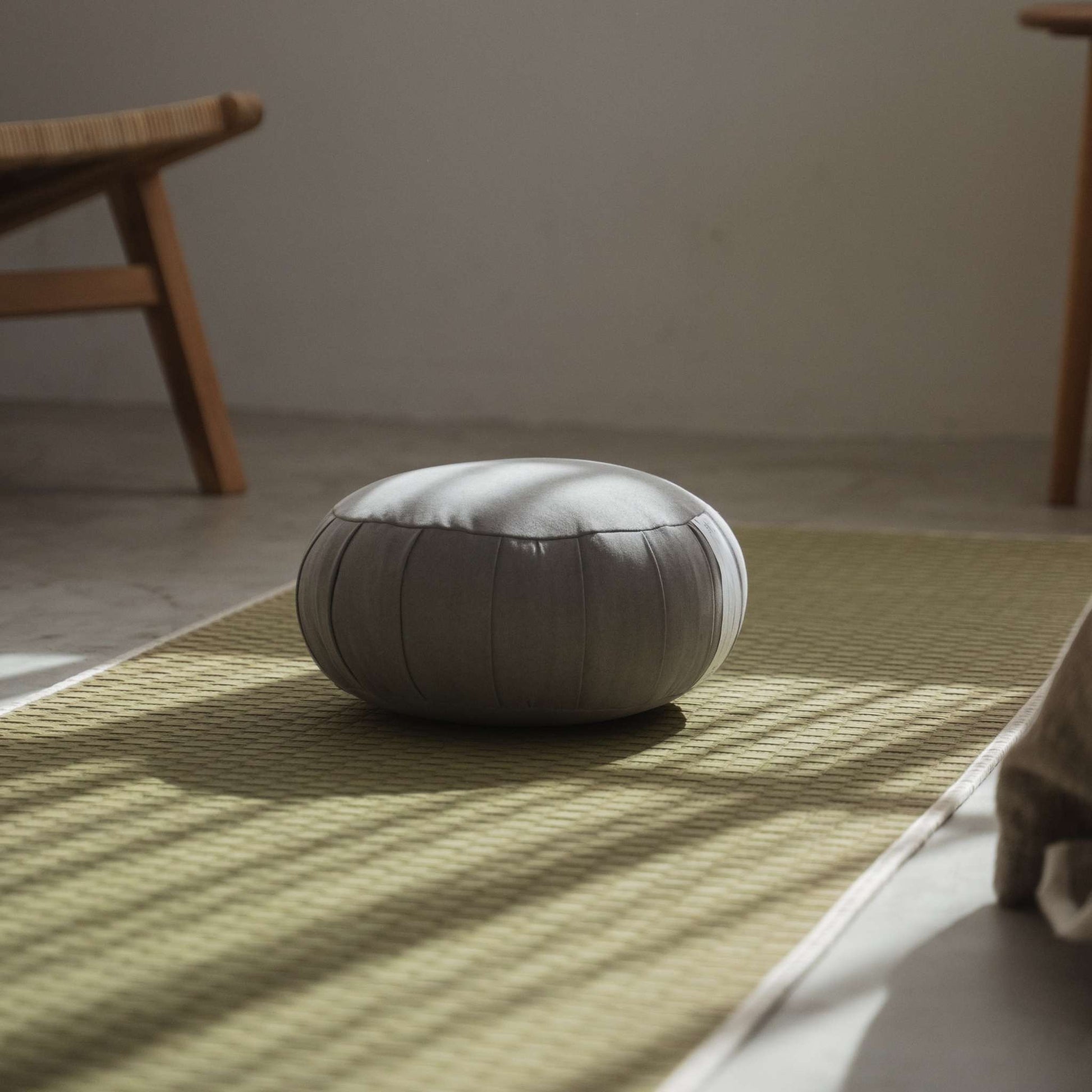 Silver gray zafu meditation cushion placed on a green tatami mat in a minimalist zen space for mindfulness.